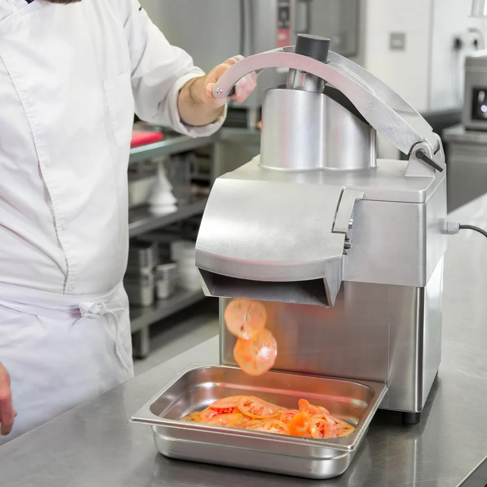 A chef lowers the pusher lever of the „Sammic“ CA-31 as tomato slices drop into a container