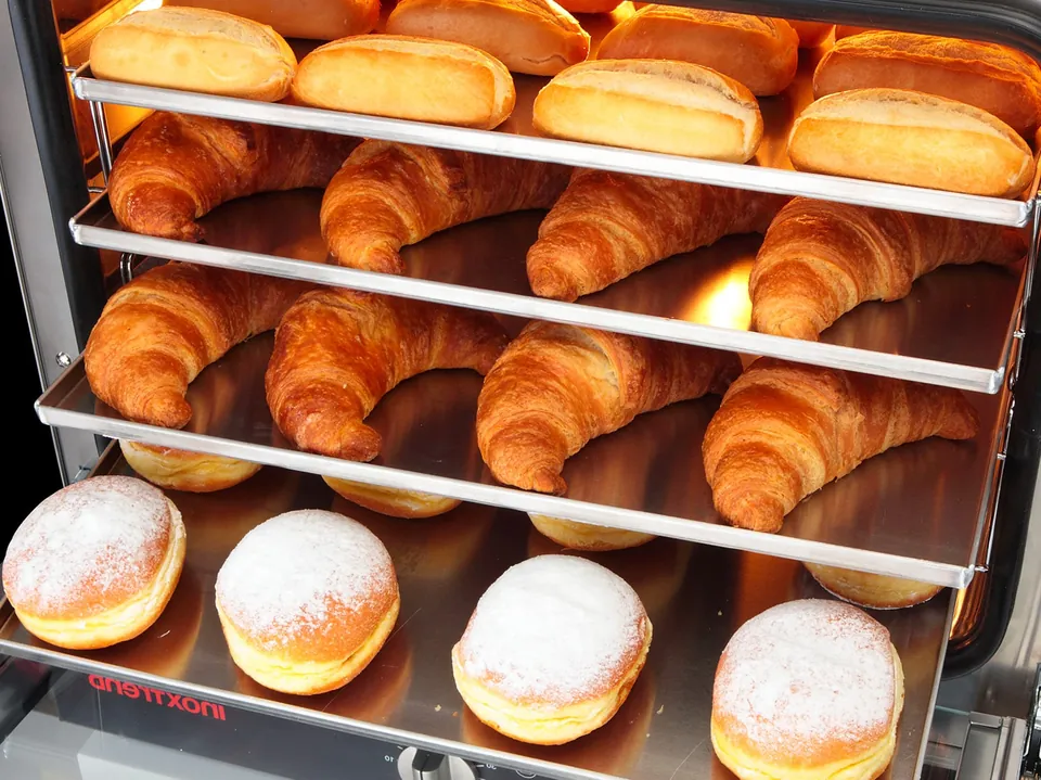 Manufacturer photo: croissants, rolls and doughnuts baking on several levels of an „Inoxtrend“ Flexo oven