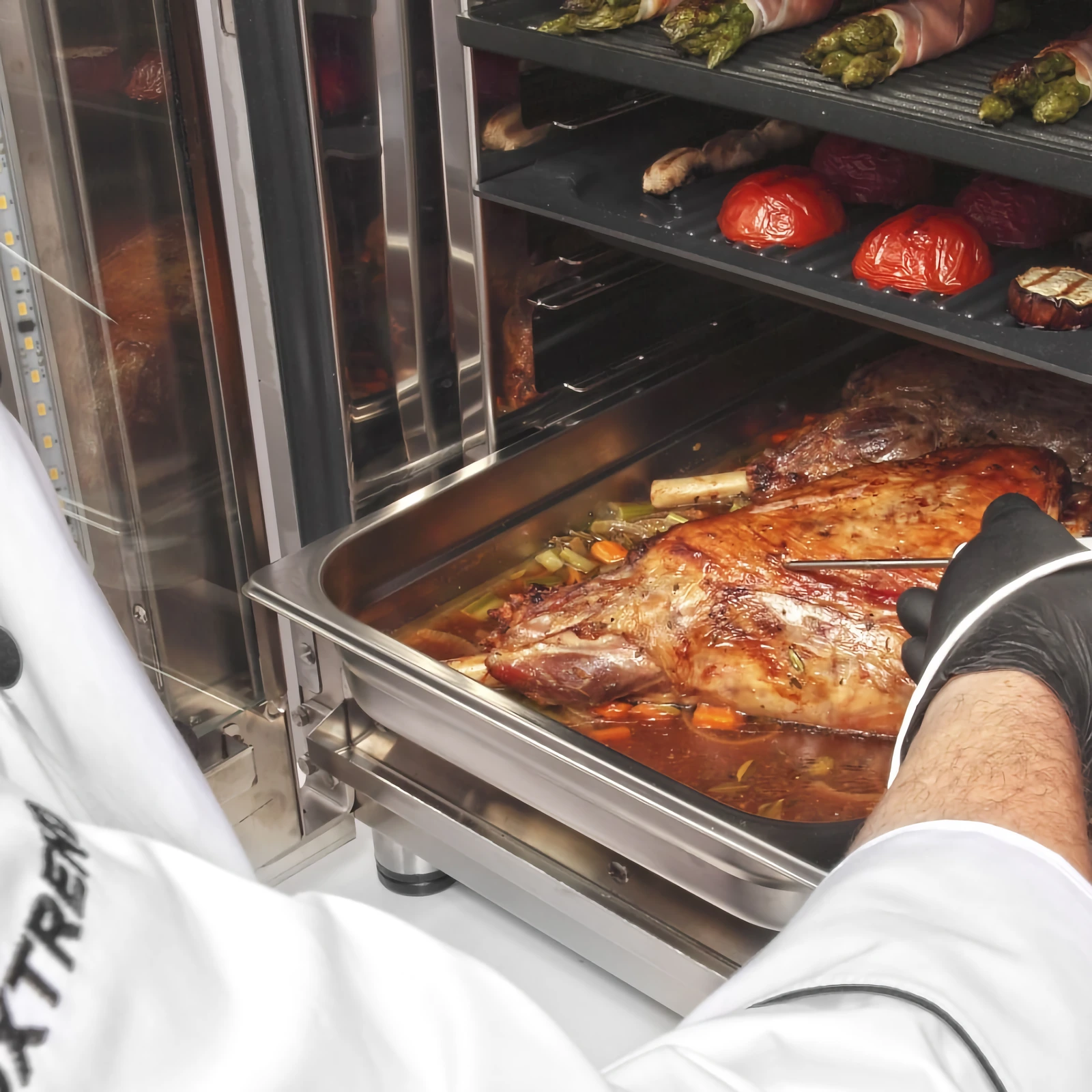 A chef takes a tray of roast meat out of an „Inoxtrend“ Level-Up oven, with vegetables cooking on the other levels